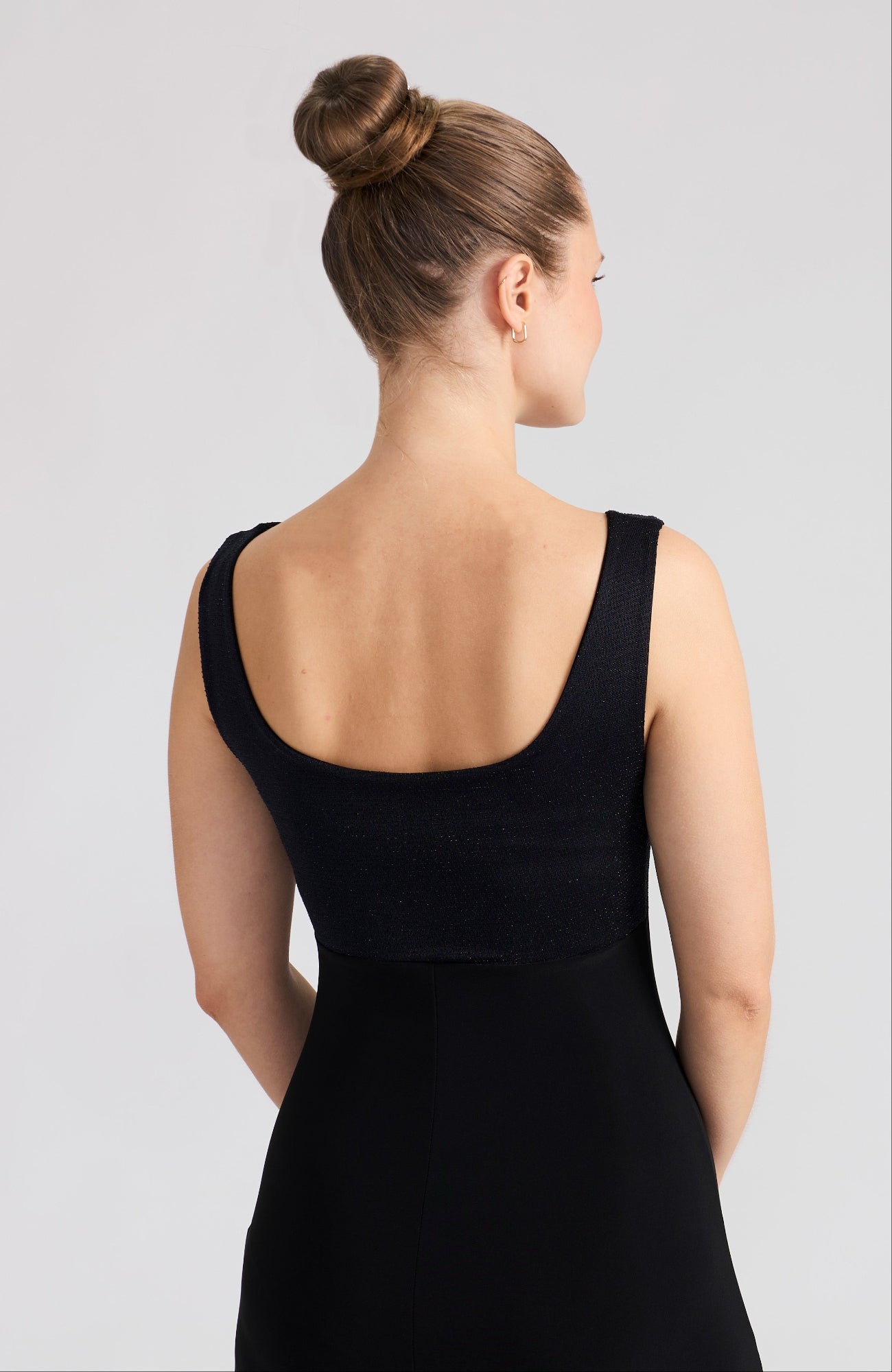 Woman wearing a black sleeveless dress against a light gray background